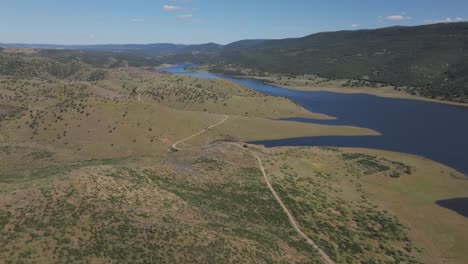 medium-height aerial shot over golden hills and trails bordering the blue cijara reservoir, fed by the guadiana river. a panoramic and cinematic view on a hot, sunny spring day in badajoz, spain.