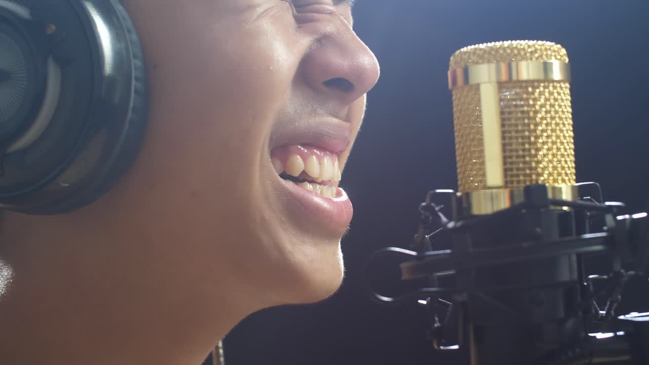 흑색 배경 에 있는 콘덴서 마이크 로 노래 하는 헤드폰 을 착용 한 젊은 아시아 소년 의 근접적 인 측면 시각