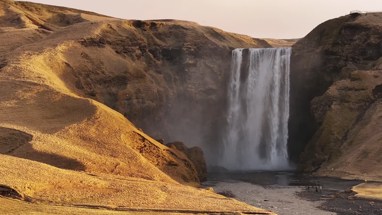 Golden hour drone view of Iceland’s Skógafoss waterfall near Eyjafjallajökull, raw cliffs, misty falls and glowing terrain in cinematic 4K.