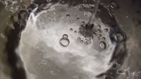 water flowing from tap into pot, vortex and bubbles on surface, close-up