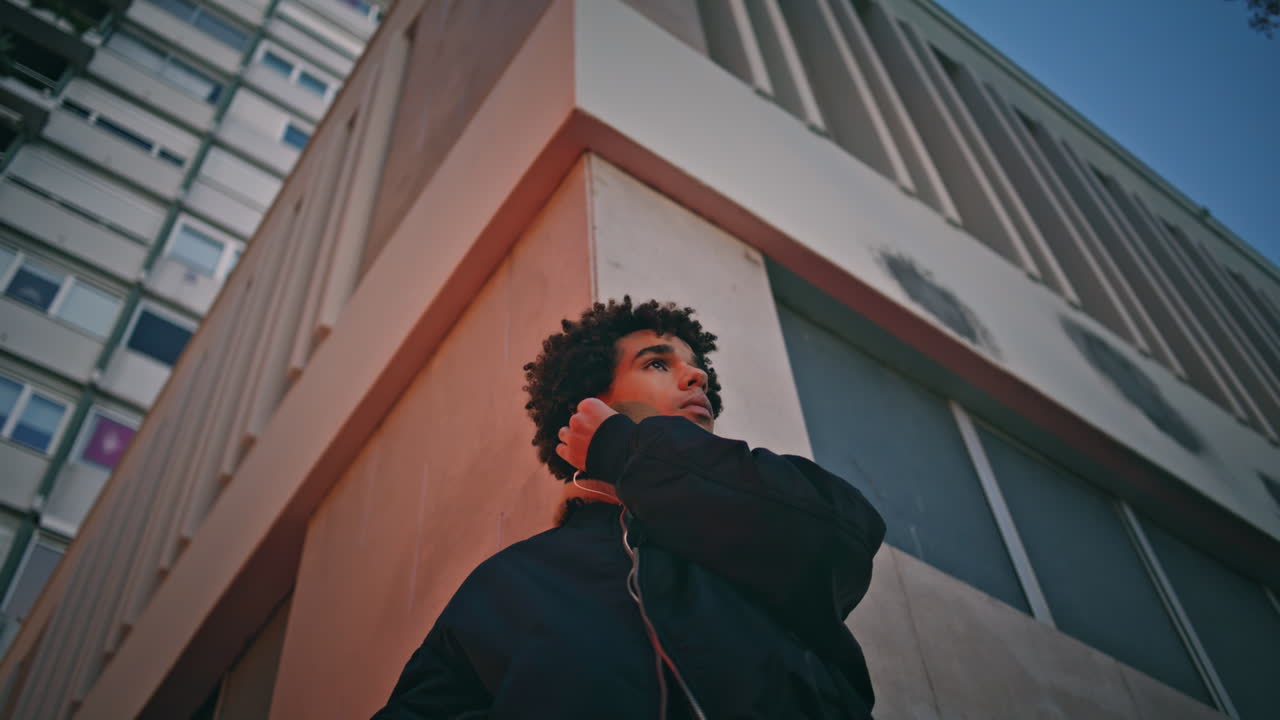 도시 건물 배경에서 이어폰을 조정하는 남자. 음악을 듣는 남자