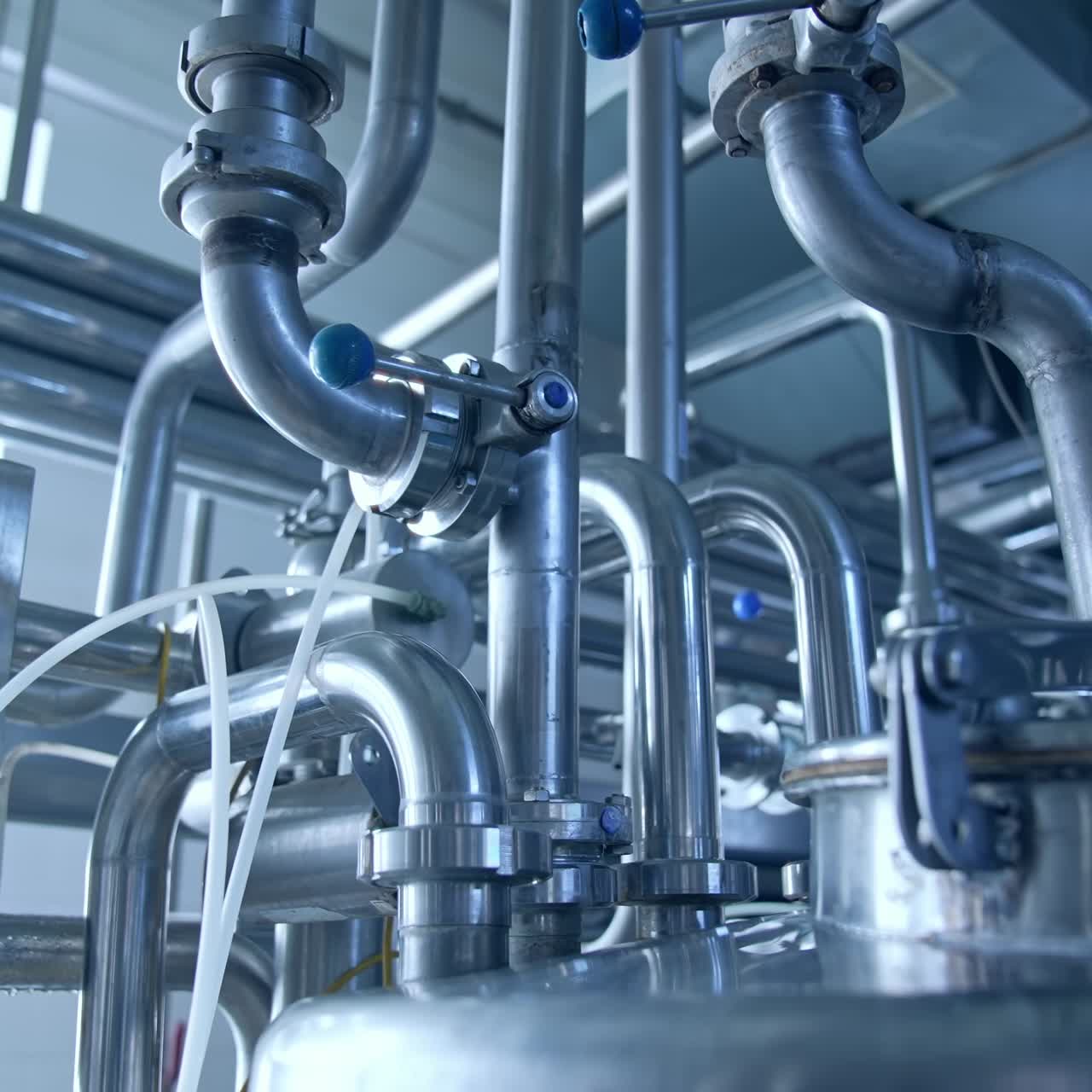 Bended pipes with sluices and faucets. Stainless steel pipe constructions at the dairy manufacturing plant. Silver pipes shining at the light from a window