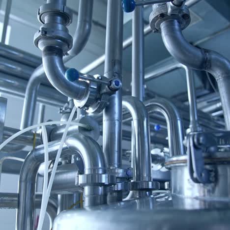 bended pipes with sluices and faucets. stainless steel pipe constructions at the dairy manufacturing plant. silver pipes shining at the light from a window