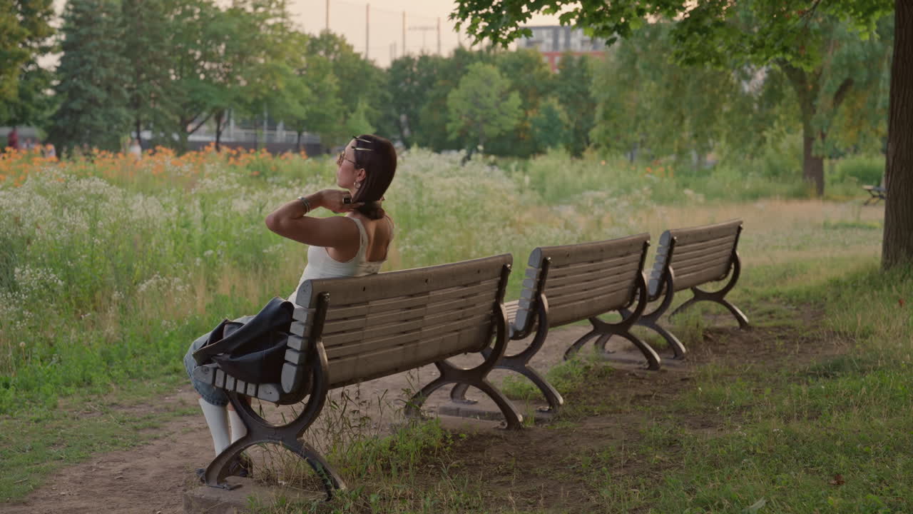 Young woman walking to sit on empty benches in park settling in with phone transitioning to journal writing