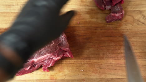 el chef está cortando en cubitos el plato de carne fresca más delicioso, usando guantes negros y un cuchillo de chef afilado