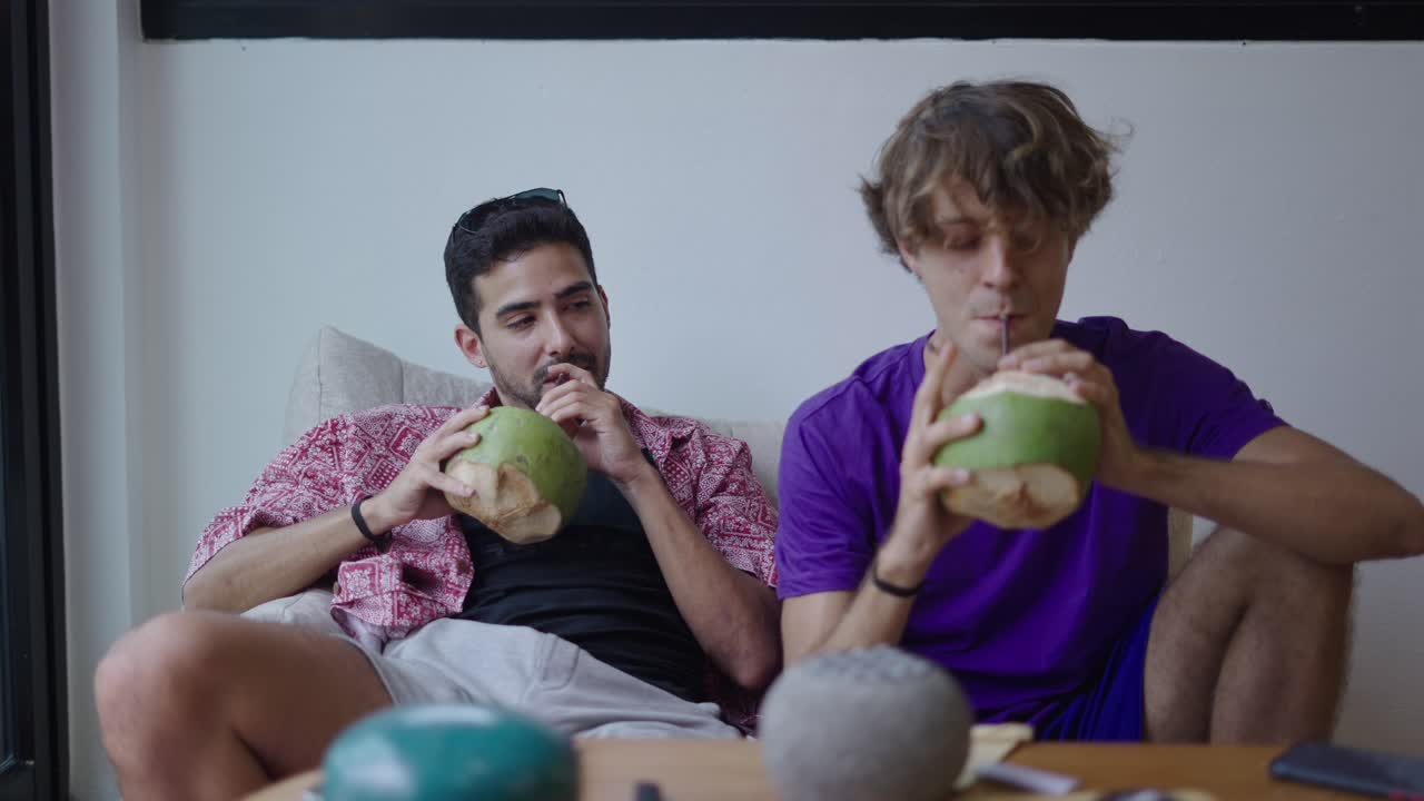 Two friends relaxing indoors and drinking fresh coconut water