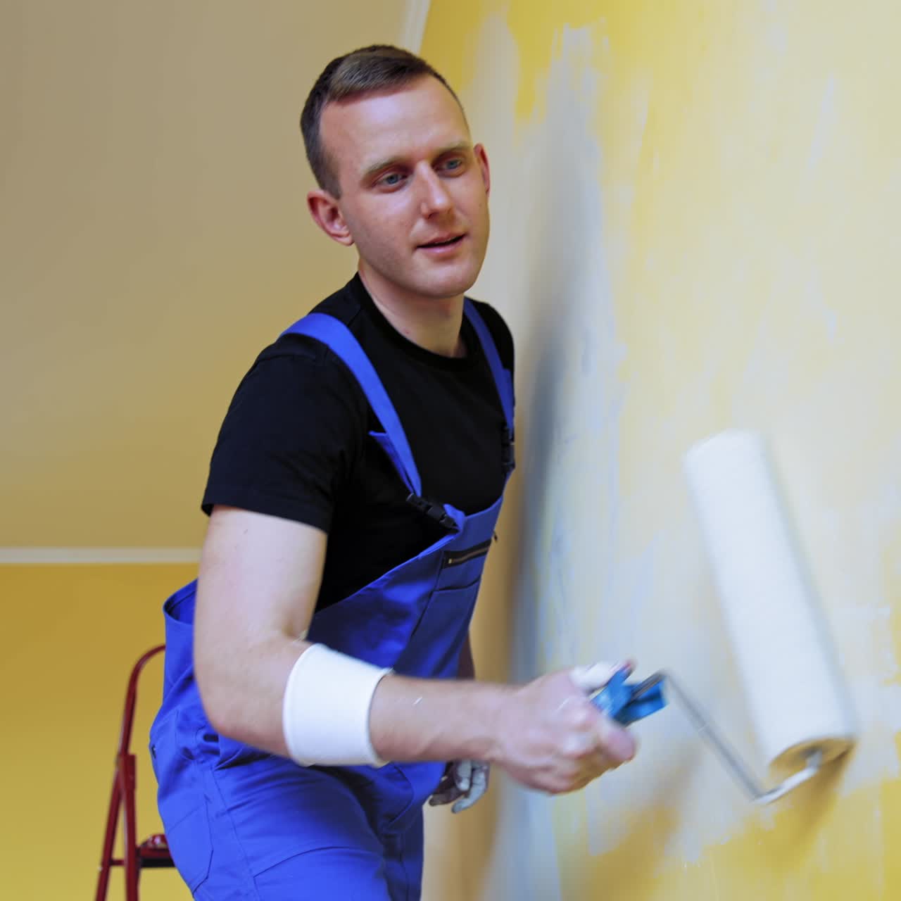 Attractive painter doing new interior of wall. Cheerful man working with paintings