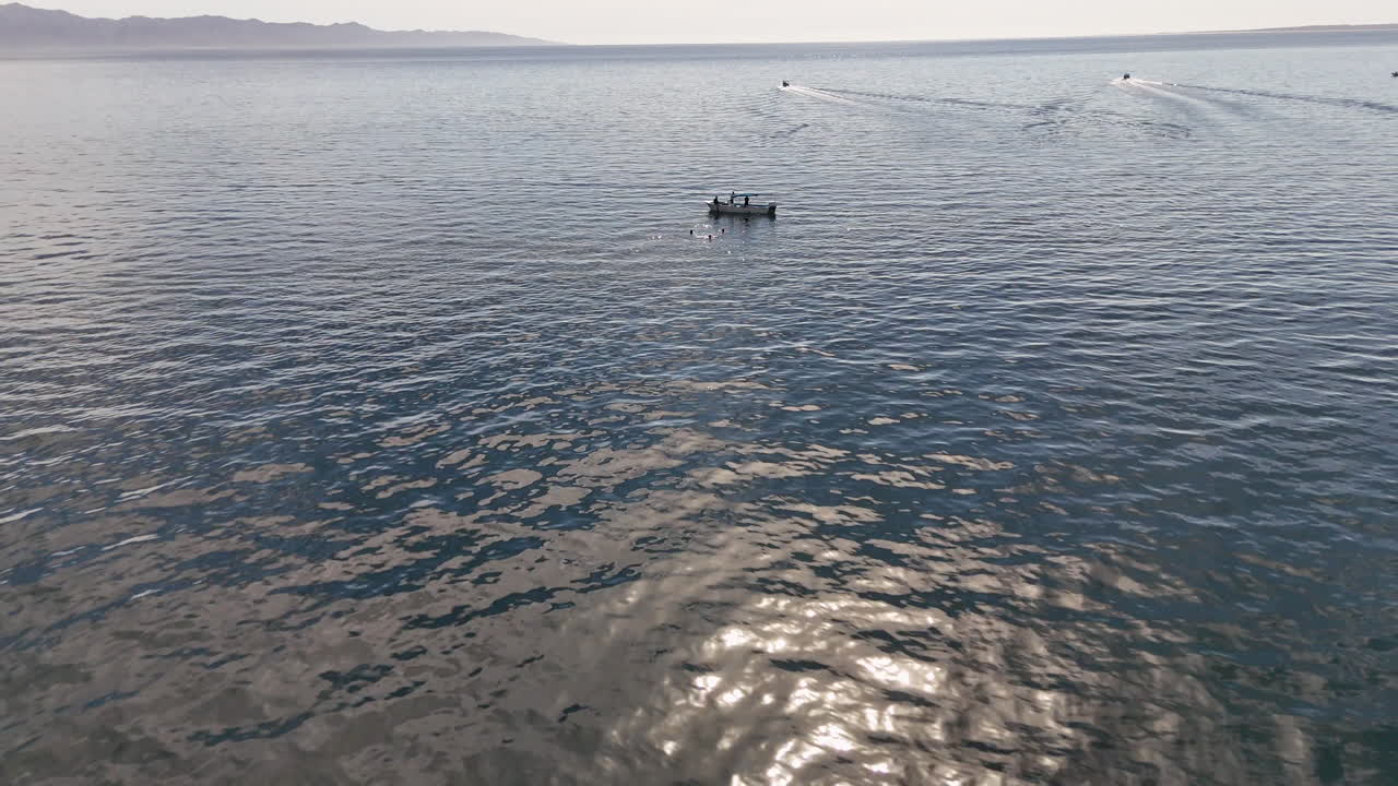 Revealing drone footage of a boat and swimmers in Baja California. Wide aerial shot.