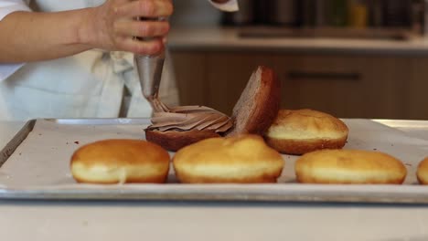 unrecognizable baker adding cream on cakes in kitchen