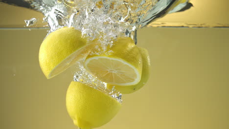 slow motion of fresh sliced lemons falling into water on yellow background