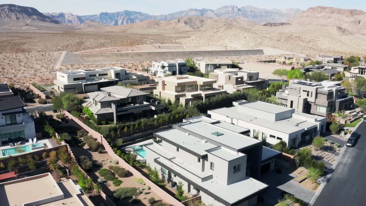 Aerial pan of sunny real estate community houses surrounded by desert mountains