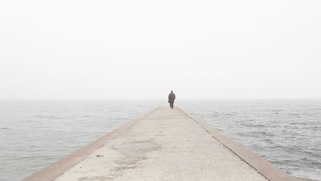 person walking on the concrete pier on a foggy day at sea