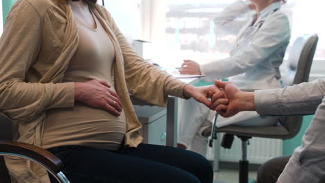 gynecologist talking to her patient in the consultation while the husband holding hands his pregnant wife