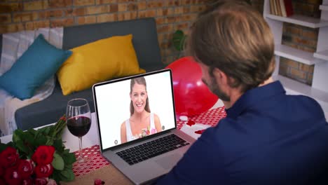 Pareja-Caucásica-En-Una-Videollamada-De-San-Valentín-Hombre-Saludando-A-Una-Mujer-Sonriente-Sosteniendo-Un-Ramo-En-El-Portátil