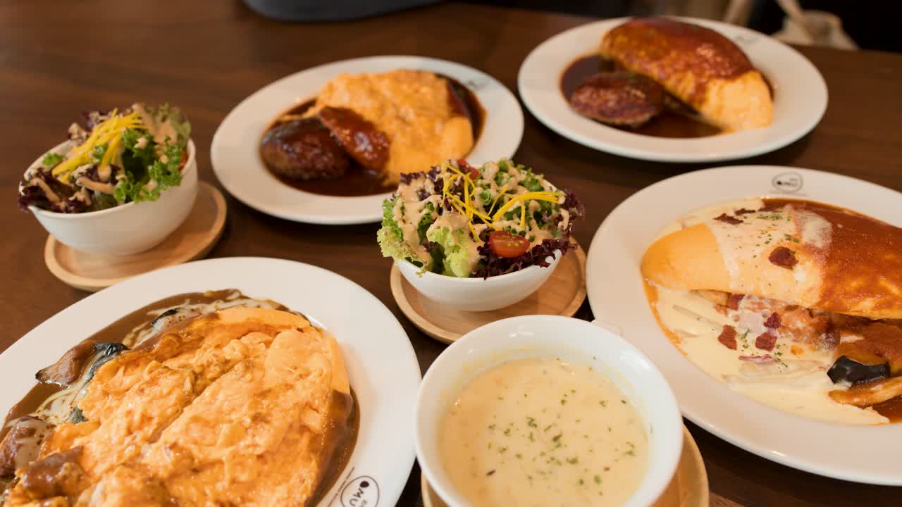 Overhead view of Japanese omelette rice, creamy soup, salad, and bread in warm restaurant lighting