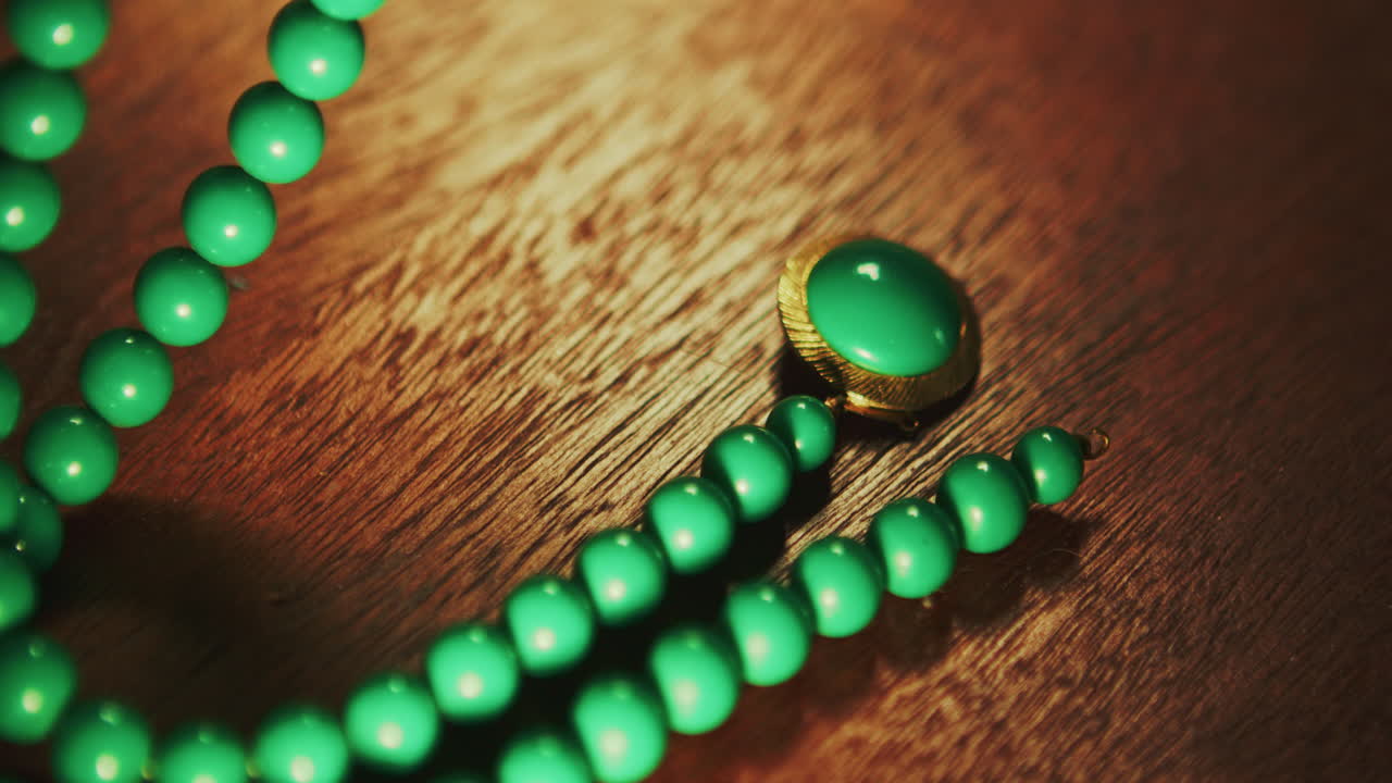 Primo piano di una collana di perline verdi appoggiata su un tavolo di legno con gioielli vintage e piccoli ninnoli. Adatta per scopi legati al patrimonio culturale, alla moda, all'uso documentaristico.