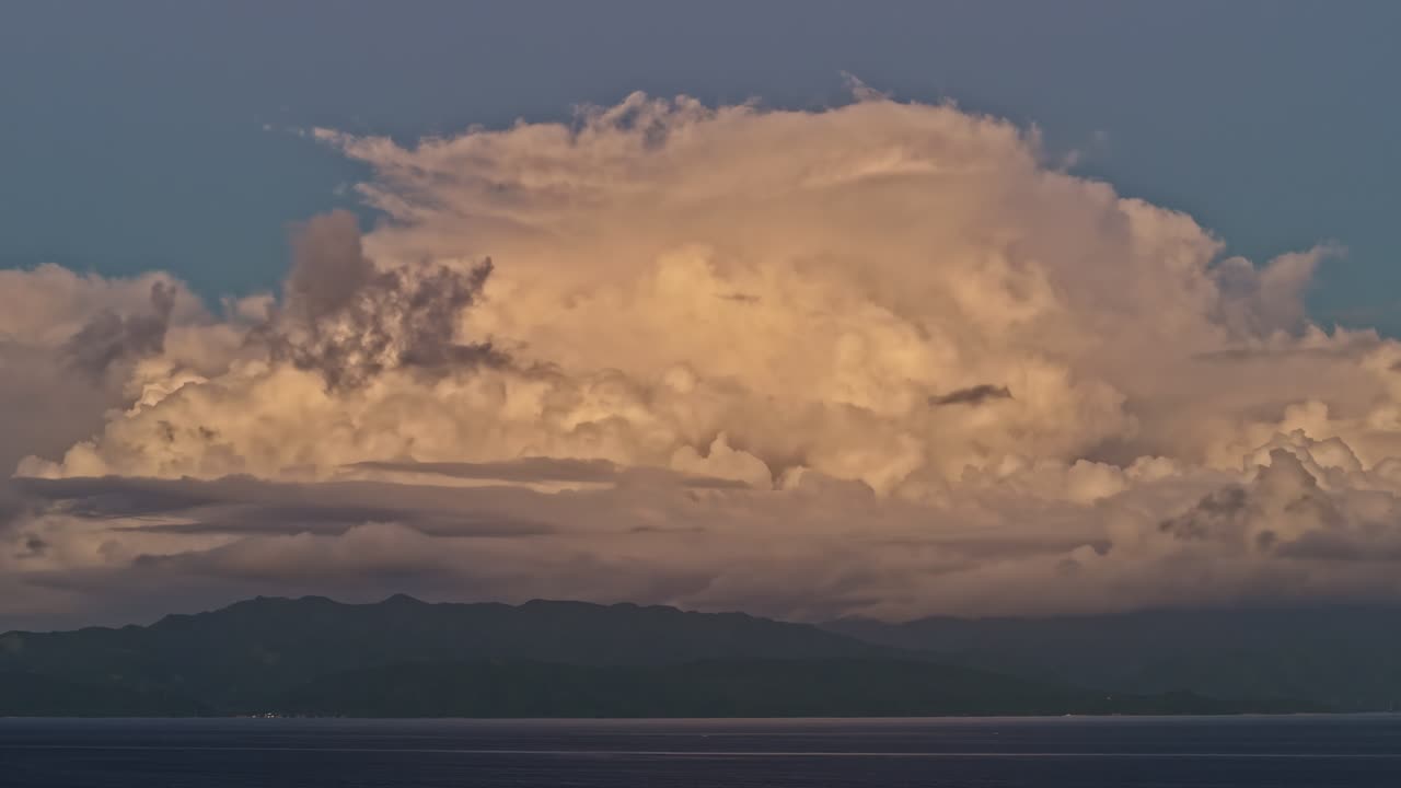 Towering clouds catch the last light of day over a tranquil bay and distant mountains