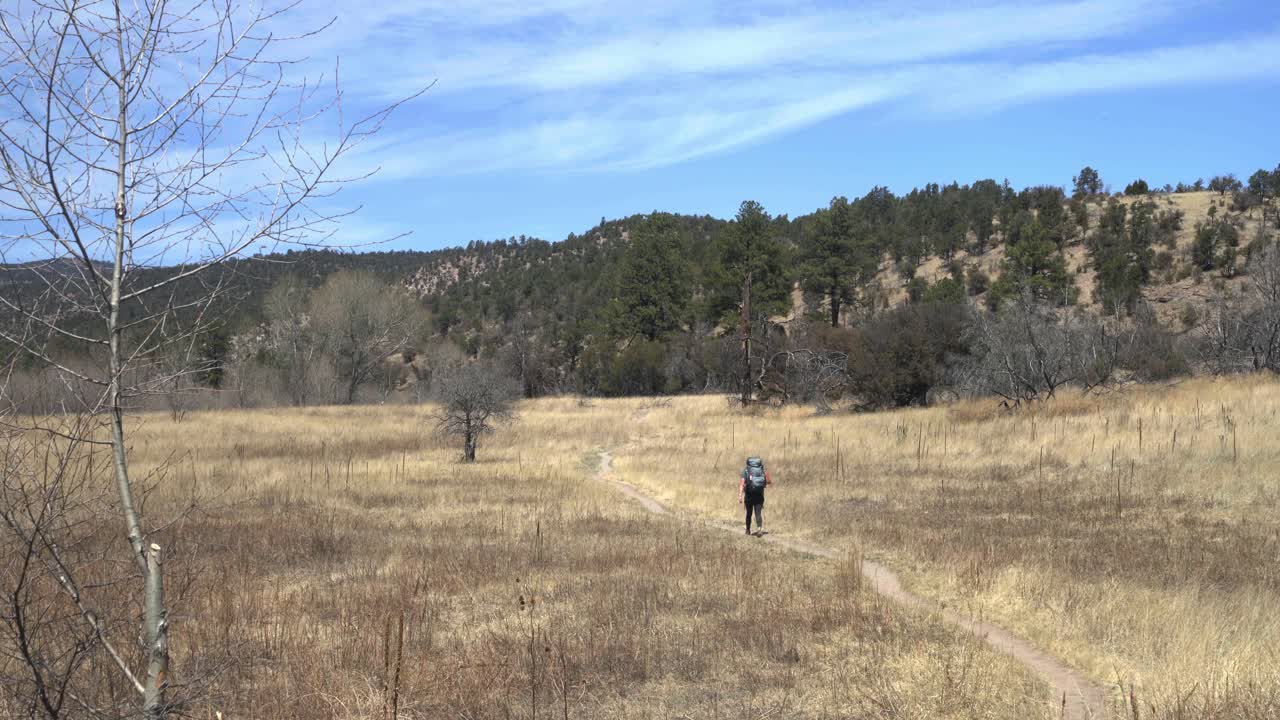 mochilera solitaria caminando a través de un prado en un sendero en un desierto remoto