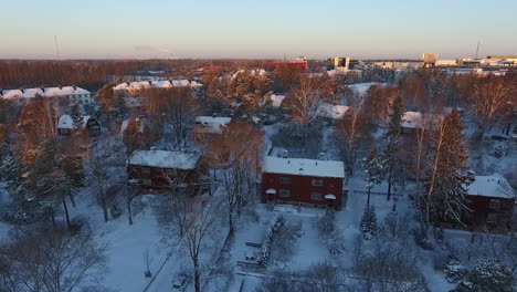 An-aerial-drone-shot,-during-sunrise,-that-slowly-pans-toward-the-left-to-reveal-views-of-a-densely-populated-urban-city-covered-in-sparkling-white-snow-during-winter