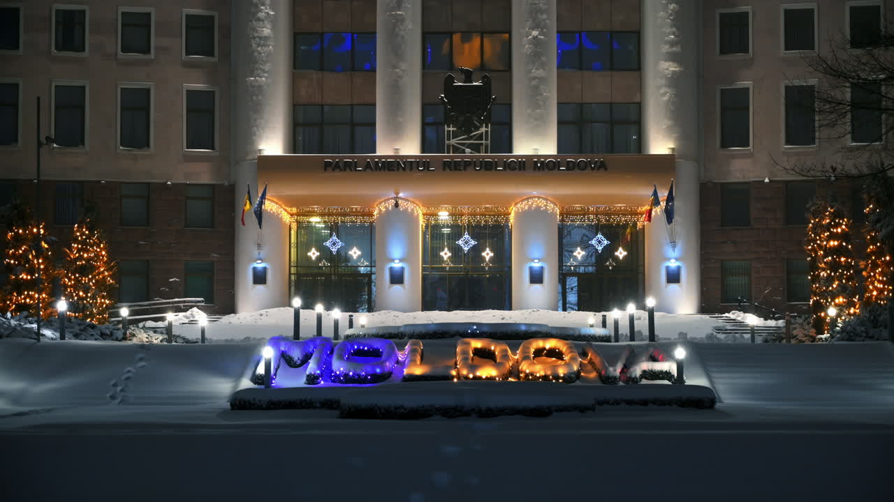 Parliament of the Republic of Moldova with national emblem, illumination and Christmas decorations in the evening. Ground covered in snow. Winter in Chisinau