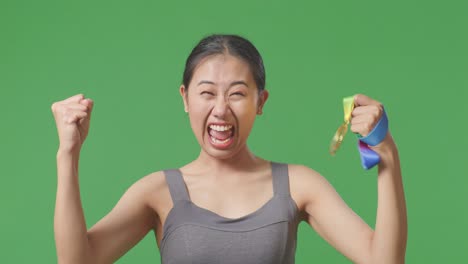 close up of asian woman wearing a gold medal and smiling to camera being proud winning as the first winner on green screen background in the studio
