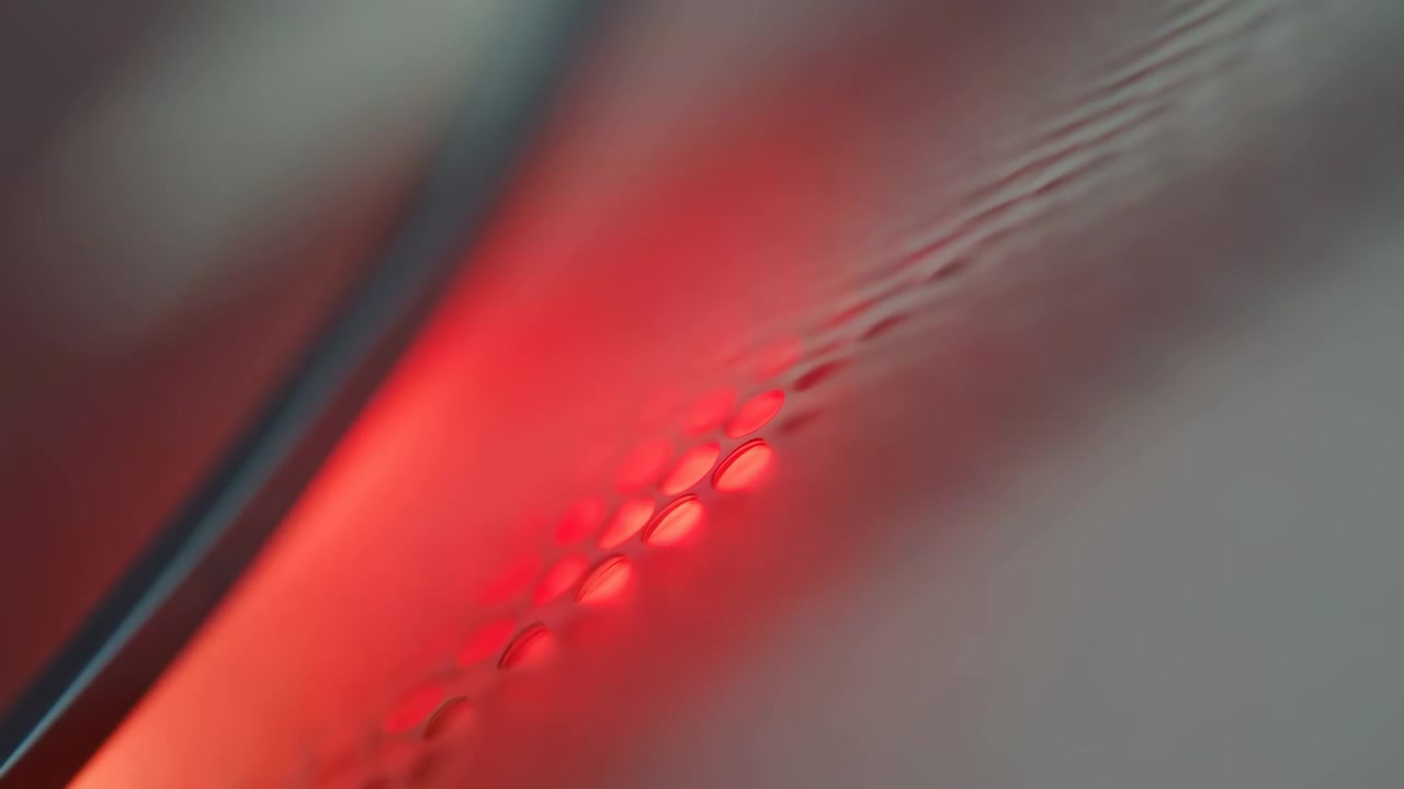 Morbida scena astratta con un vivido bagliore rosso vicino al centro-sinistra, toni grigi sfocati intorno ad esso, un bordo diagonale scuro in primo piano e sottili increspature.