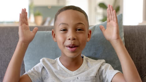young african american boy covering his eyes with his hands while sitting on couch