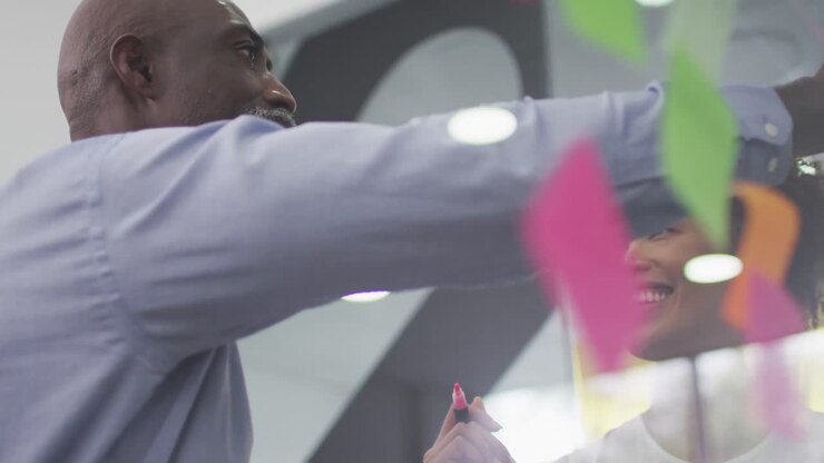 Diverse businessman and businesswoman brainstorming and smiling by transparent board with memo notes