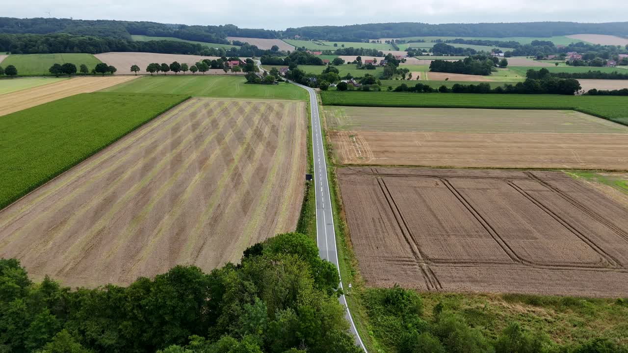 Hauptstraße, umgeben von landwirtschaftlichen Feldern und Hügeln an einem bewölkten Sommertag. Amerikanisches ländliches Vorstadtgebiet. Weitwinkel-Luftaufnahme nach vorne. Ruhige und malerische Landschaft in den Vereinigten Staaten.
