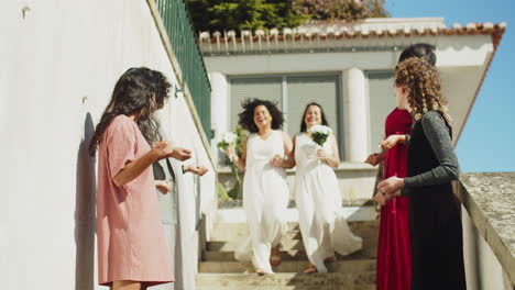 bridesmaids waiting for lesbian couple after wedding ceremony and throwing rice over happy newlyweds while they descending stairs and kissing