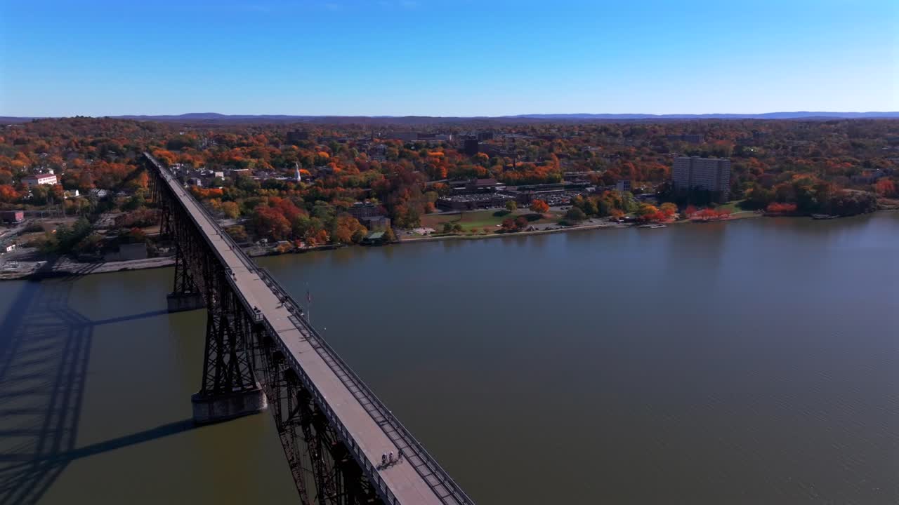 An aerial view of the Hudson River, flying over the Walkway Over the Hudson State Park bridge on a sunny day in autumn. The camera dolly in, pan left over it then dolly out from the large footbridge.