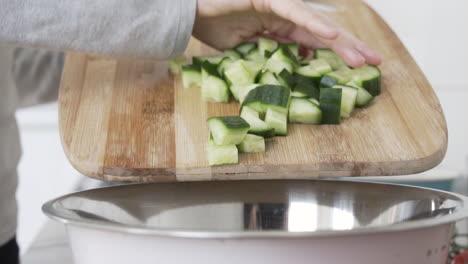 Mano-Poniendo-Rodajas-De-Pepino-Picadas-En-Un-Tazón-De-La-Tabla-De-Cortar