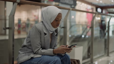 Black-woman-with-hijab-and-cellphone-rests-in-trade-mall