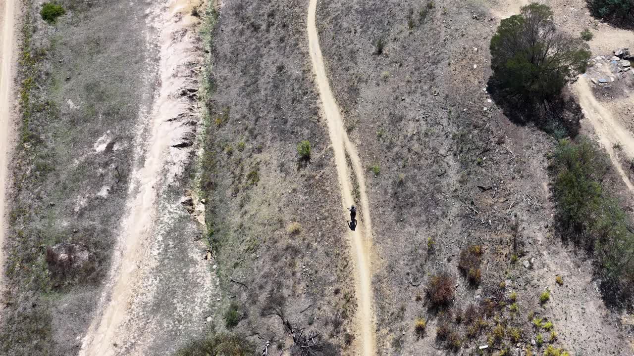 Ripresa aerea dall'alto con drone che segue un ciclista che attraversa un paesaggio arido di bushland australiano