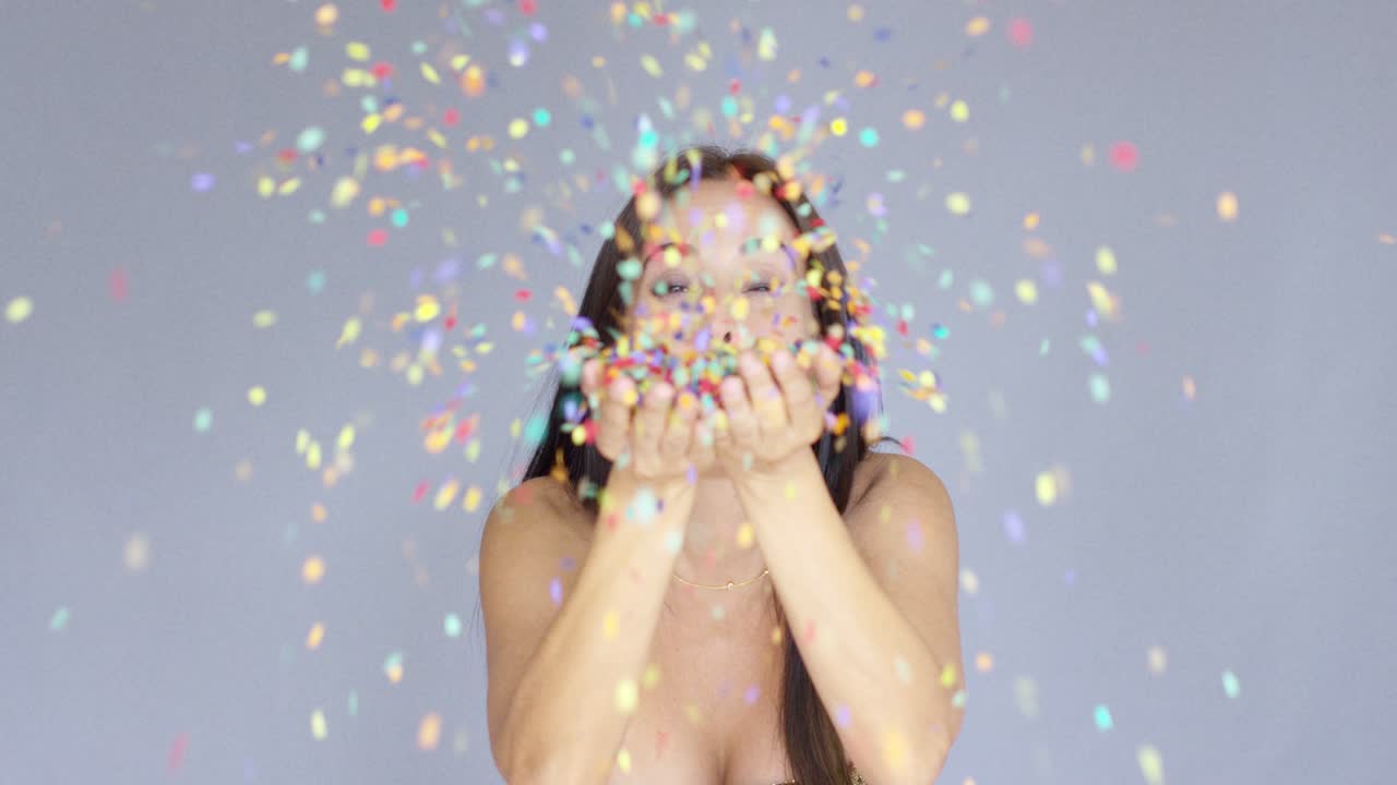 Giovane donna che soffia coriandoli colorati di Capodanno