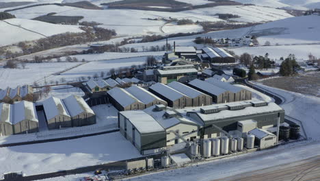 aerial view of the glenlivet whisky distillery surrounded by snow in the late afternoon sun on a winters day, moray, scotland - rising shot