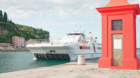 piran, slovenia - jul 03 2023: a catamaran traveling from piran to venice docks next to the red lighthouse on the pier