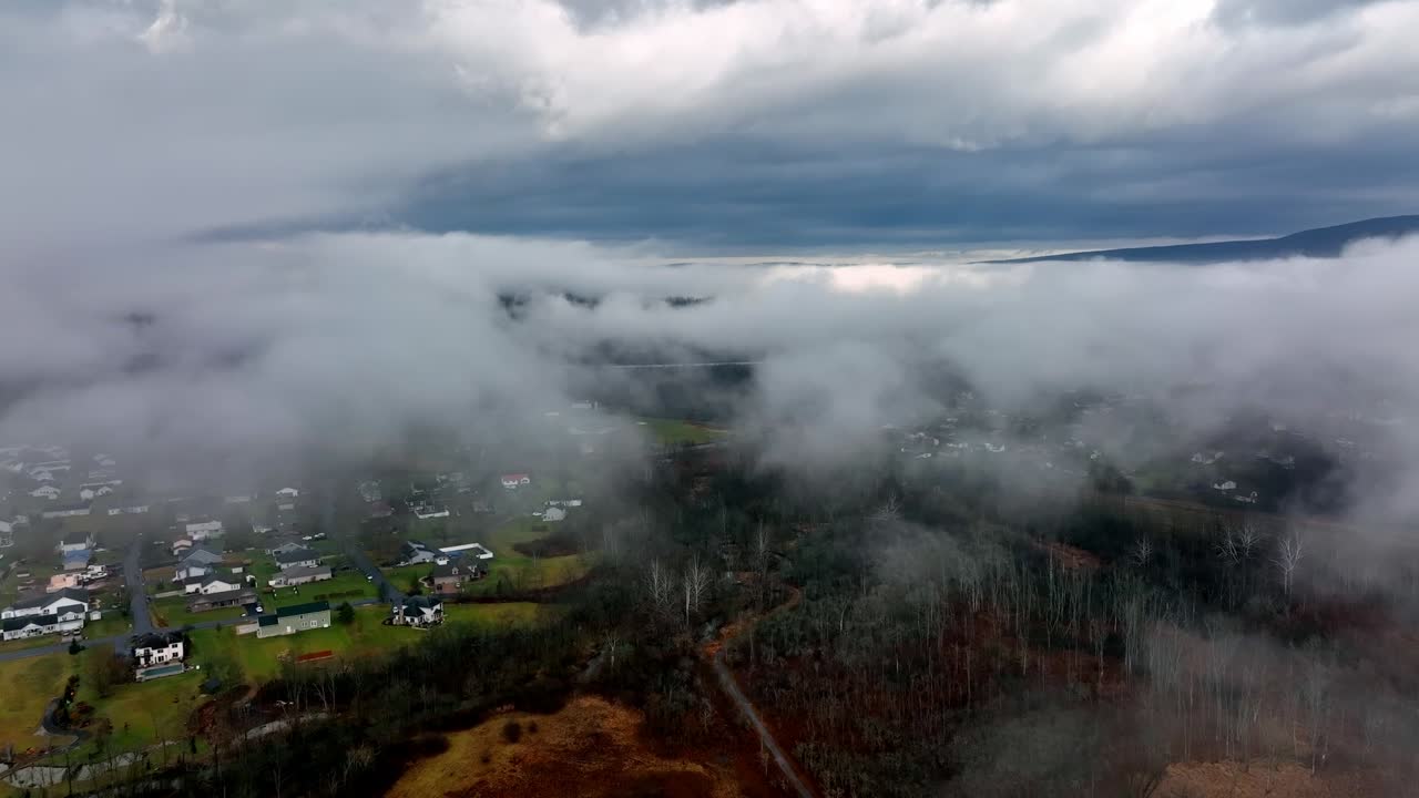 Drone flying over rural landscape in the midst of low-level clouds.