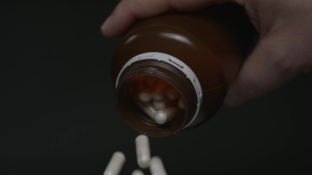 Capsules spilling from a brown prescription bottle in slow motion. Studio close-up with black background and pharmaceutical concept.