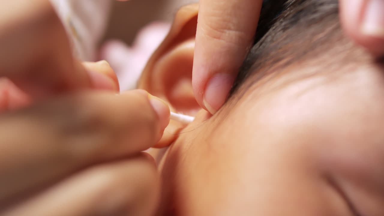 A mother tenderly cleans her baby's ear showcasing the importance of gentle care.
