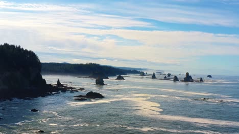 stunning trucking right aerial drone shot of the gorgeous third beach in forks, washington with large rock formations, cliffs, small waves and sea foam on a warm sunny summer morning