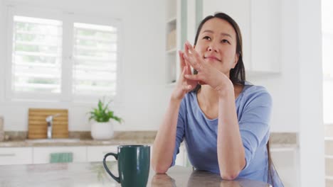 happy asian woman sitting in kitchen and drinking coffee