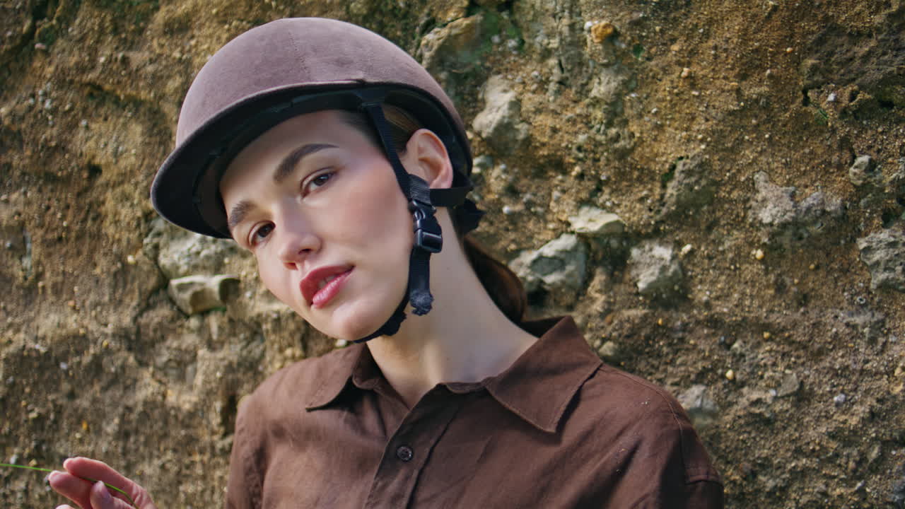 Portrait equipped horsewoman posing near stoned wall. Woman playing spikelet