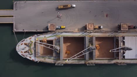 vista aérea de un buque de carga lleno de trigo descargando su carga en camiones de carga en un muelle comercial