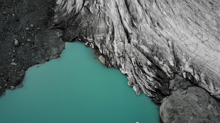 Sorvolo aereo sopra il lago glaciale turchese presso il ghiacciaio Hohlaub vicino a Saas-Fee nel Vallese, Svizzera, con una panoramica verso l'alto da una vista dall'alto dell'acqua fino ai crepacci di ghiaccio e alle cime delle montagne