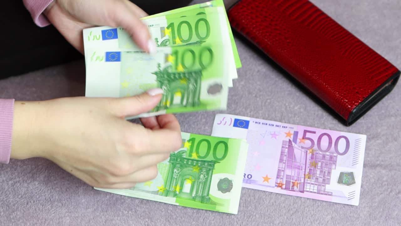 la chica se sienta cuenta dinero por 100 euros, 500 euros y una billetera roja yace cerca.