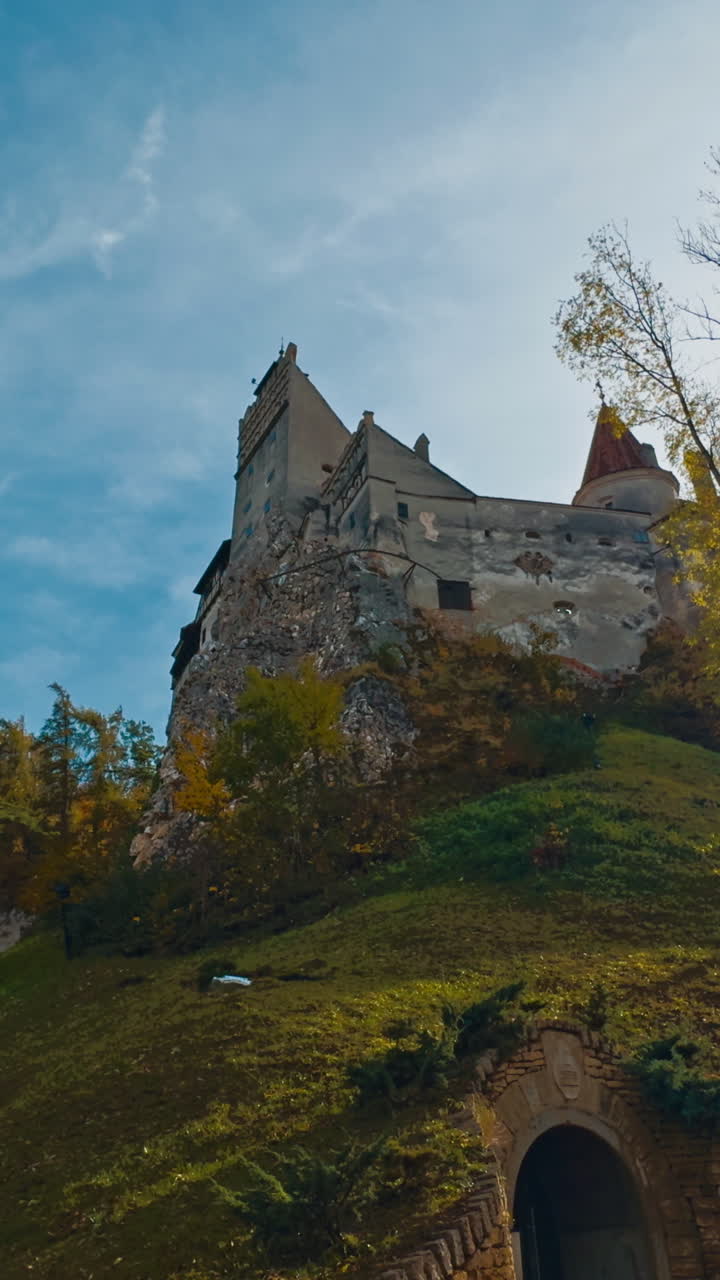 Secret entrance to the castle standing on the high hill. Low angle view on Bran Castle in colorful autumn season. Vertical video