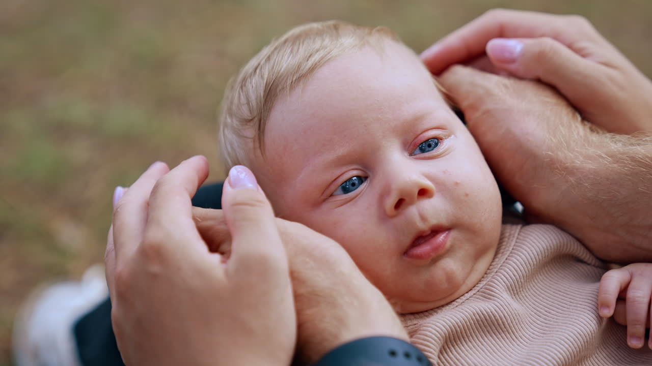 Hands of parents hold the head of baby from both sides. Blue-eyed blonde kid's portrait. Close up.
