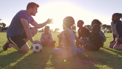 young school kids and teacher sitting with ball in field