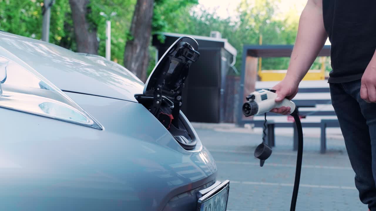 proceso de reabastecimiento de combustible de un automóvil eléctrico. un disparo debajo de la escotilla donde se carga el automóvil ecológico eléctrico. la escotella de carga del automóvil eléctrico se abre automáticamente. una mano masculina inserta un automóvil erecto